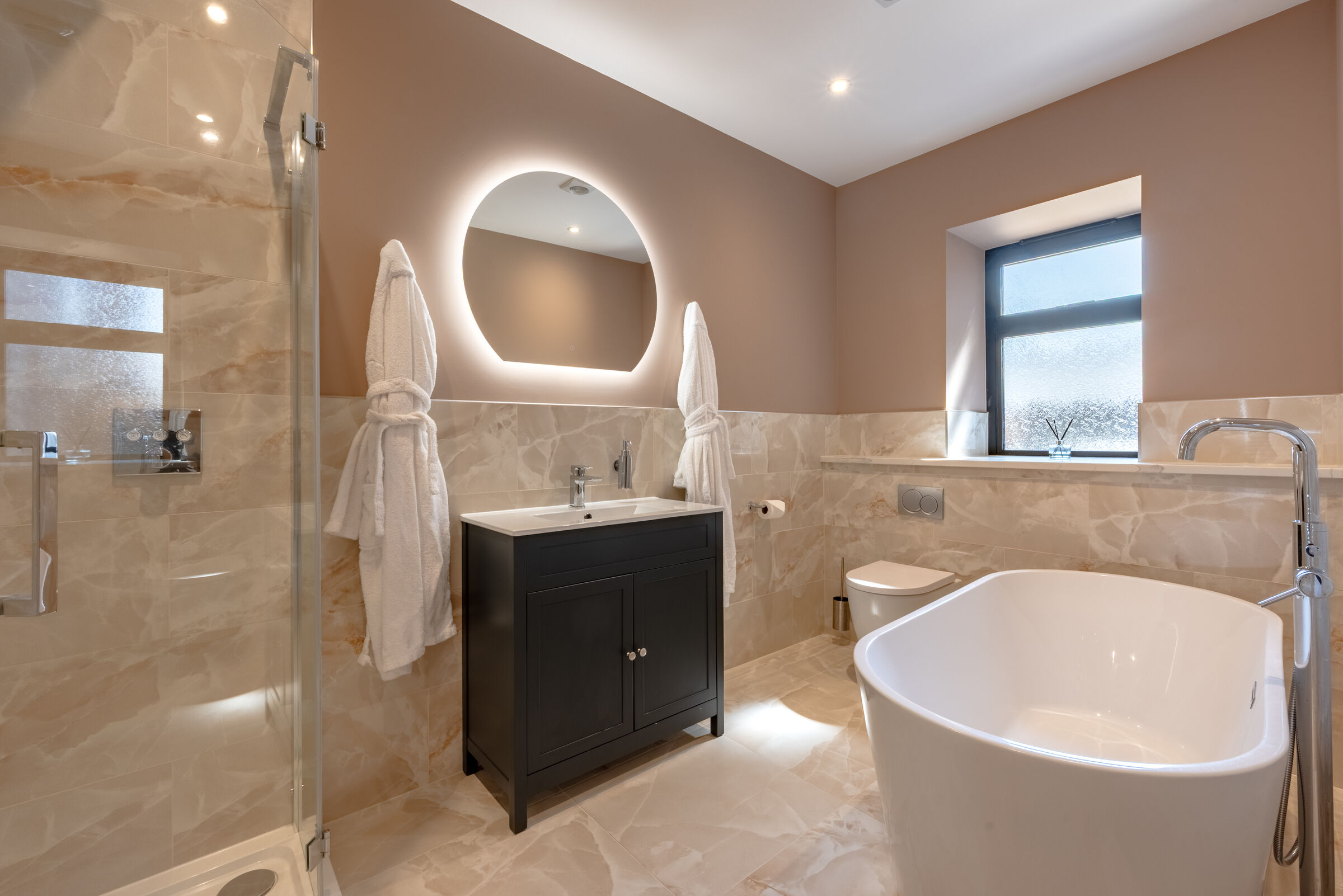 Freestanding bath beneath a backlit mirror